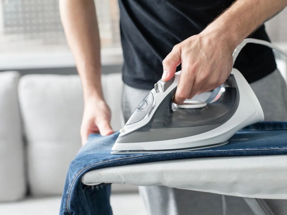 Persona planchando cuidadosamente la pernera de un pantalón de vestir sobre una tabla