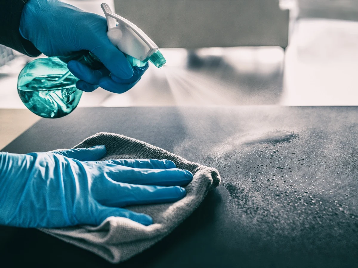 Person wearing gloves disinfecting a door handle with a spray and cloth