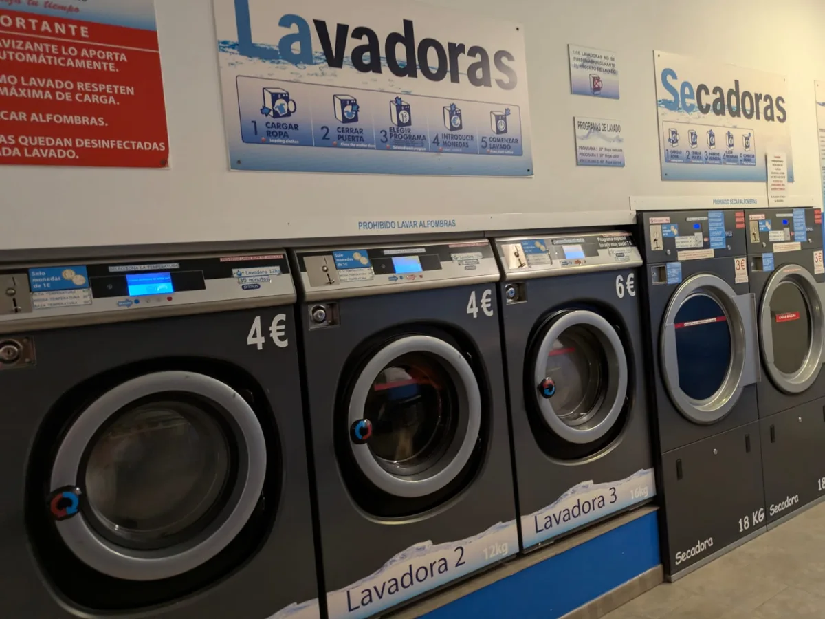 Interior de lavandería autoservicio mostrando una lavadora cargada correctamente frente a una sobrecargada