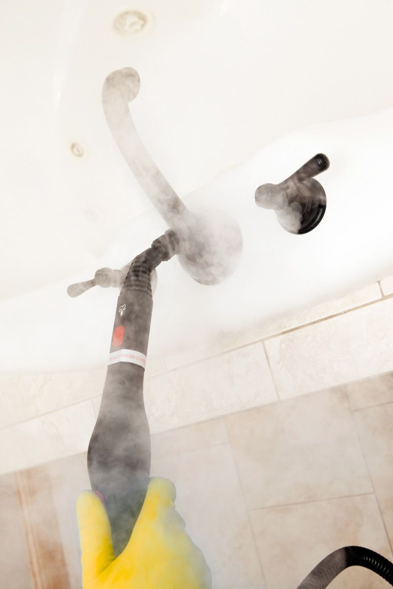 Mano con guante limpiando una bañera con una vaporeta o maquina de limpieza a vapor.