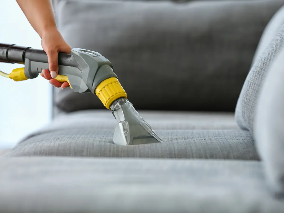 Cleaning a beige sofa with an injection-extraction machine showing dirty water being sucked up